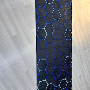 May include: A black and blue geometric rug with a honeycomb pattern. The rug has a distressed look, with faded areas in the black background.