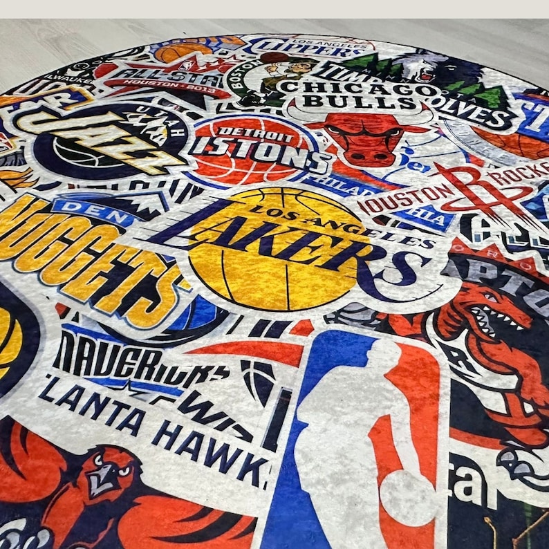 May include: A colourful rug featuring a variety of NBA team logos, including the Lakers, Nuggets, Bulls, Pistons, and Hawks. The rug is made from a soft, plush material and features a range of colours, including red, blue, yellow, and white.