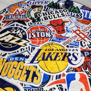 May include: A colourful collage of NBA team logos, including the Utah Jazz, Detroit Pistons, Chicago Bulls, Los Angeles Lakers, Denver Nuggets, and Houston Rockets. The logos are arranged in a circular pattern on a white background.