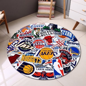 May include: A round rug with a white background and a colourful design of various NBA team logos. The logos are arranged in a random pattern and include teams like the Lakers, Celtics, Bulls, and Rockets.