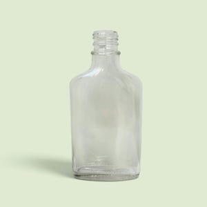 May include: A clear glass bottle with a rounded rectangular body and a narrow, threaded neck designed for a screw-on cap. The bottle features smooth, transparent walls and a flat base, showcasing a simple, functional design for liquid storage.