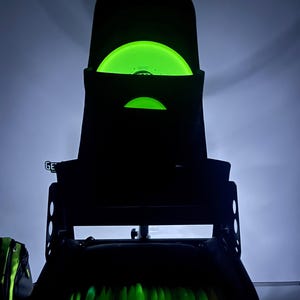 Puede incluir: Una bolsa negra de disco de golf con un disco verde que brilla en la oscuridad en el bolsillo superior. La bolsa tiene varios bolsillos y una correa. La bolsa est&aacute; llena de m&aacute;s discos que brillan en la oscuridad.