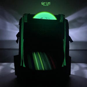Puede incluir: Una bolsa negra de disco de golf con un disco que brilla en la oscuridad en su interior. La bolsa tiene una correa verde y el texto "GET LIT!" est&aacute; impreso en la parte superior de la bolsa.