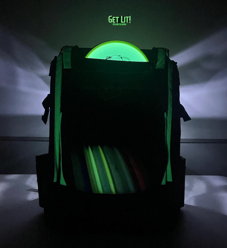 Puede incluir: Una bolsa negra de disco de golf con un disco que brilla en la oscuridad en su interior. La bolsa tiene una correa verde y el texto "GET LIT!" est&aacute; impreso en la parte superior de la bolsa.