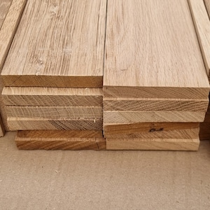 May include: A stack of unfinished, light brown wood planks. The planks are stacked on a brown surface.