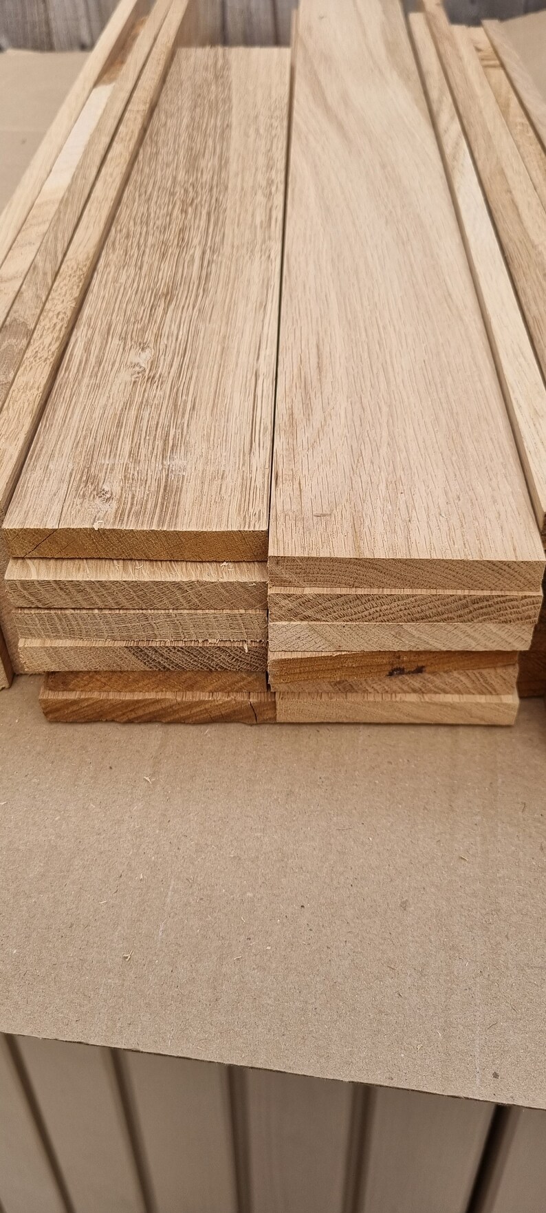 May include: A stack of unfinished, light brown wood planks. The planks are stacked on a brown surface.