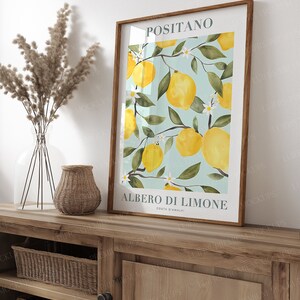 May include: A framed print with a watercolor illustration of a lemon tree with yellow lemons and white flowers. The print has the text "Positano" and "Albero di Limone Costa d'Amalfi" in a white font.