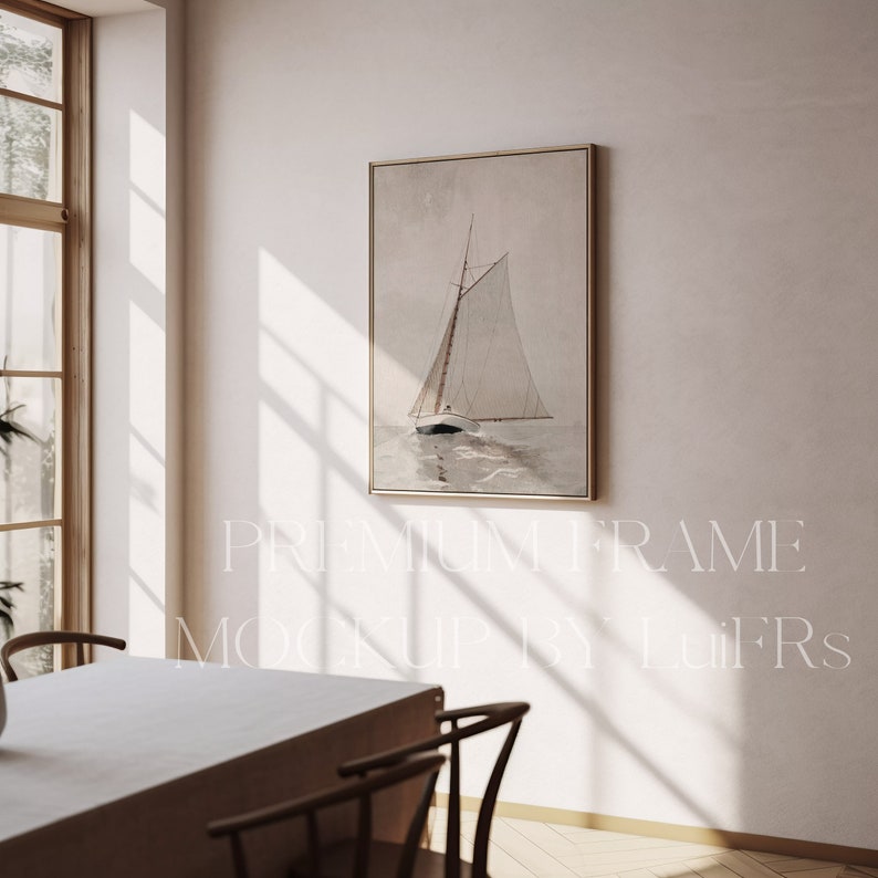 May include: A framed print of a sailboat on the water with a light brown background. The frame is a light gold color and the print is hanging on a white wall. The print is in a room with a wooden table and chairs.