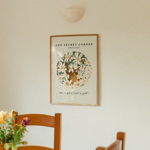 May include: A framed print with a white background and a circle of white flowers with a deer in the center. The text "THE SECRET GARDEN" and "SOAK IT ALL IN" is at the top of the print. The text "You've got a heart of gold." is at the bottom of the print.