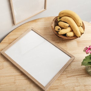 Könnte beinhalten: Ein Holztisch mit einem weißen Rahmen, eine Schüssel mit gelben Bananen und eine Topfpflanze mit rosa Blüten.