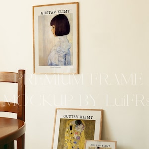 Op de afbeelding: Drie ingelijste prints van schilderijen van Gustav Klimt. De bovenste print toont een portret van een vrouw met kort donker haar. De middelste print toont een schilderij van twee figuren die elkaar omhelzen, bekend als "De Kus". De onderste print toont een schilderij van een groep mensen in een kleurrijk, geometrisch patroon.