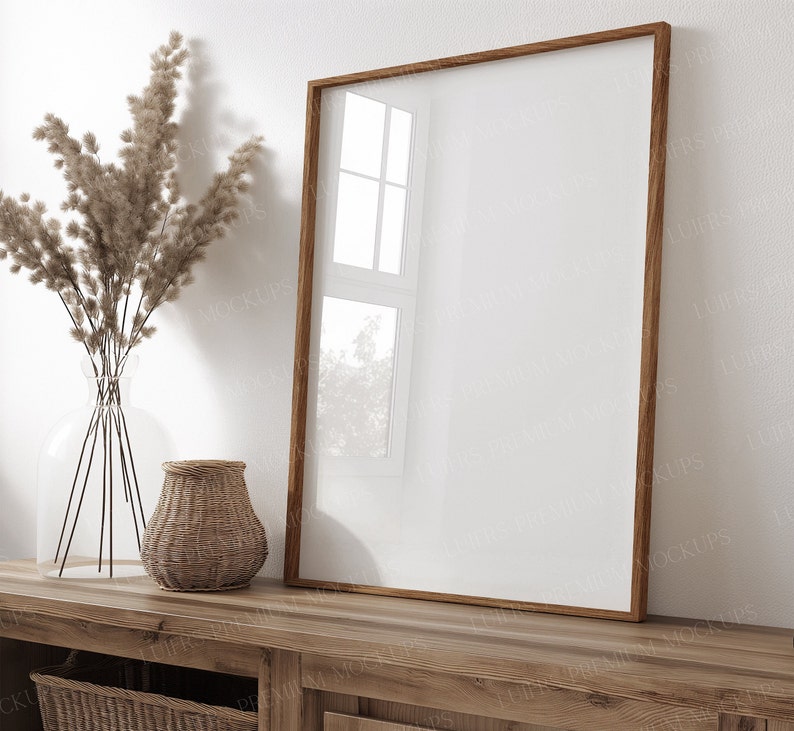 May include: A wooden frame with a blank white canvas inside, sitting on a wooden table with a vase of dried pampas grass and a woven basket.