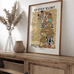 May include: A framed print of Gustav Klimt's "The Tree of Life" painting. The painting features a couple embracing in a colorful, abstract style with a gold background. The frame is brown wood with a white mat.