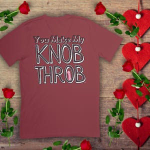 May include: A maroon t-shirt with the text "You Make My KNOB THROB" in black and white with a pink heart graphic.