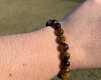 May include: A brown and gold beaded bracelet made of tiger's eye stones.