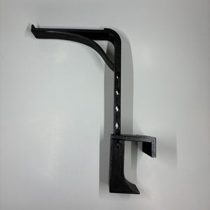 May include: A black, 3D-printed shelf bracket with a curved support arm and a vertical support with multiple mounting holes. The bracket has a small shelf at the bottom and is designed for wall mounting.