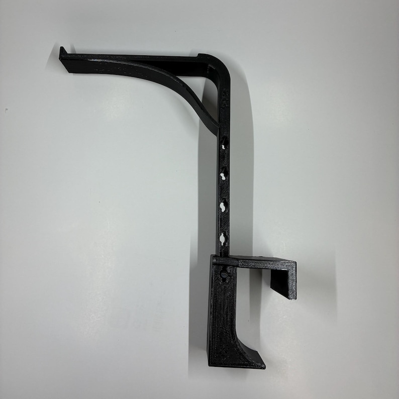 May include: A black, 3D-printed shelf bracket with a curved support arm and a vertical support with multiple mounting holes. The bracket has a small shelf at the bottom and is designed for wall mounting.