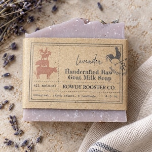 May include: A rectangular bar of lavender-scented goat milk soap wrapped in a tan paper label. The label features the text Lavender, Handcrafted Raw Goat Milk Soap, Rowdy Rooster Co., and 4.3 oz, along with illustrations of farm animals.