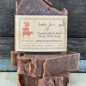 May include: A stack of three rectangular bars of brown goat milk soap. The top bar features a tan paper label with the text Pumpkin Spice Latte, Handcrafted Raw Goat Milk Soap, Rowdy Rooster Co., and 4.3 oz, alongside a graphic of stacked farm animals.