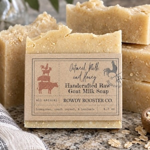 May include: A rectangular bar of beige oatmeal, milk, and honey goat milk soap wrapped in a brown paper label. The label features a rooster, pig, and cow illustration with the text: Oatmeal, Milk, and Honey, Handcrafted Raw Goat Milk Soap, Rowdy Rooster Co., all natural, homegrown, ranch raised, & handmade, 122g.