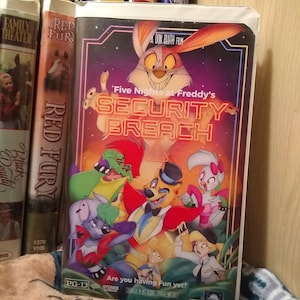 May include: VHS tape for "Five Nights at Freddy's: Security Breach" with colorful cartoon characters. The cover features a rabbit, bear, and other figures against a purple and orange background. The text "Are you having Fun yet?" is also visible.