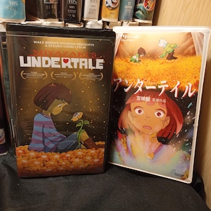 May include: Two VHS tapes featuring animated films. One tape has the title "Miyazaki's Undertale" with a character holding a flower. The other tape has Japanese text and a colorful illustration of a woman with red hair.