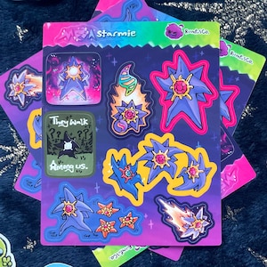 Könnte beinhalten: Ein Bogen bunter Aufkleber mit sternförmigen Designs mit rosa, blauen und orangefarbenen Akzenten. Die Aufkleber enthalten den Text "Starme" und "They Walk Among Us."