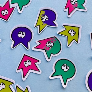 Puede incluir: Un conjunto de pegatinas de estilo caricatura con diseño de bocadillo. Las pegatinas presentan una variedad de colores, incluyendo rosa, verde, amarillo y morado, con contornos blancos y ojos saltones. Las pegatinas están dispersas sobre una superficie azul claro.