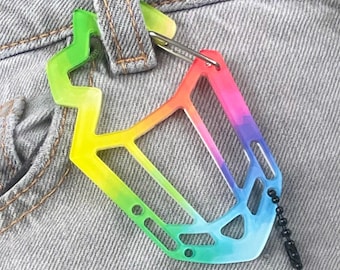 Könnte beinhalten: Ein mehrfarbiges, verlaufendes Accessoire im Karabiner-Stil mit einem geometrischen, offenen Rahmendesign, das von Limettengrün und Gelb zu Orange, Pink, Violett und Blau übergeht. Es enthält eine Metallbefestigungsschlaufe und eine schwarze Kugelkette.