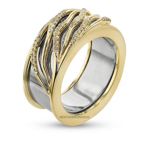May include: A wide two-tone ring featuring a polished silver-colored inner band and a yellow gold-colored outer band. The gold section is decorated with three wavy, raised lines encrusted with small clear stones. The text NEXTDIAMONDSCO is visible.