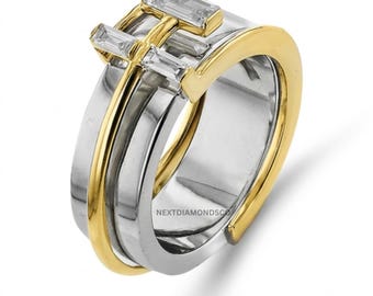 May include: A two-tone ring featuring a silver-colored band layered with a gold-colored band. The top of the ring is adorned with three baguette-cut clear stones arranged in a horizontal row. The text NEXTDIAMONDSCO is visible on the inner band.