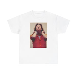 Puede incluir: Una camiseta blanca con una imagen impresa de una mujer con un mono naranja y una cadena alrededor del cuello.