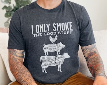May include: A dark heather grey t-shirt with a white graphic of a pig, chicken, and cow with labeled cuts of meat. The text "I Only Smoke The Good Stuff" is printed on the shirt.