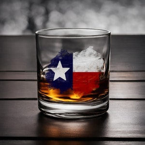 Puede incluir: Un vaso de whisky con un cubito de hielo con la bandera de Texas. El cubito de hielo está parcialmente derretido, revelando los colores rojo, blanco y azul de la bandera.