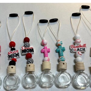 May include: A collection of clear glass car air fresheners with decorative beads and charms. Charms include a pig, crosses, baseballs, and text that reads "Band Mom", "Dance Mom", "Baseball Coach", and "Stand and Thrive".