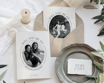 May include: A white card with black text that reads "Will you be my bridesmaid?" with a black and white photo of two women in the center. The date "09.07.2024" is printed at the bottom of the card.