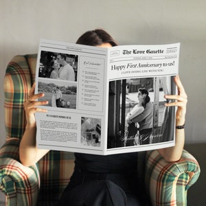 May include: A black and white newspaper with the headline "The Love Gazette" and the text "Happy First Anniversary to us! I LOVE DOING LIFE WITH YOU". The newspaper features photos of a couple.