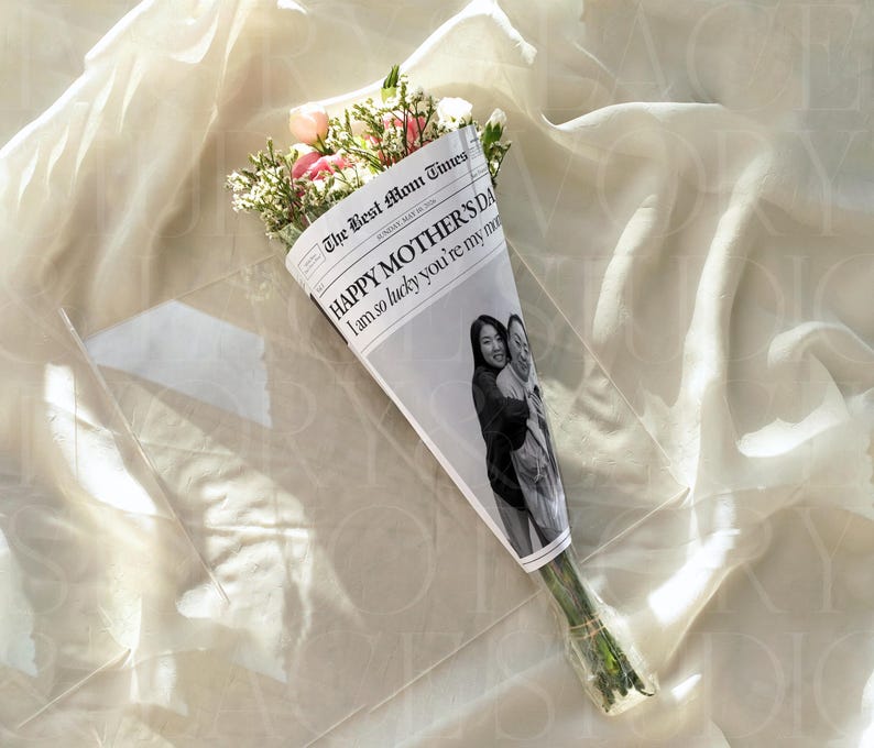 May include: A bouquet of flowers wrapped in a newspaper-style paper with the text "HAPPY MOTHER'S DAY I am so lucky you're my mom". The bouquet includes pink and white flowers and greenery. A black and white photo of two people is printed on the paper.