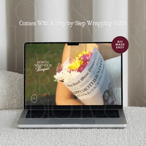 May include: A laptop displays a bouquet of flowers wrapped in newspaper, with text that reads "HOW TO WRAP YOUR BOUQUET". The screen also shows "The Best Mom Times" and "HAPPY MOTHER'S DAY". The laptop is on a white surface, with the text "Comes With A Step-by-Step Wrapping Guide".