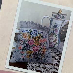 May include: A printed image of a cross-stitch project featuring a floral design with pink, yellow, and blue flowers. The image is on a cream-colored background with the text "Pochette Vintage 2" and "Reflets de Soie". A decorative teapot is also visible.