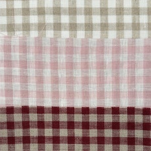 May include: Close-up of three fabric swatches with a gingham pattern. The top swatch is tan and white, the middle is pink and white, and the bottom is burgundy and white. The fabric has a woven texture.