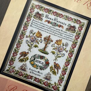Könnte beinhalten: Gerahmtes Kreuzstich-Exemplar mit floralen und Vogelmotiven. Das Exemplar enthält den Text "Bons Parents" und weiteren französischen Text. Das Design umfasst Häuser, Segelboote und einen Blumenkranz. Das Exemplar ist in einem schwarzen Rahmen.