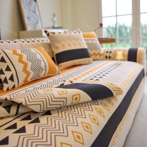May include: A white sofa with black and yellow geometric patterned throw cushions and a matching throw blanket. The sofa is covered in a white and black geometric patterned throw blanket.