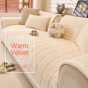 May include: Cream-coloured sofa with a textured, quilted cover and matching cushions. The words "Warm Velvet" are displayed in a white box. A small teacup and saucer sit on the sofa.