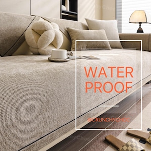 May include: Beige waterproof sofa cover with a textured weave. The cover has a dark trim and is accessorized with matching pillows and a decorative accent pillow. The text "WATER PROOF" is displayed on the cover.