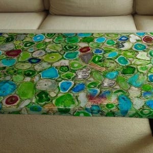Könnte beinhalten: Ein rechteckiger Couchtisch mit einer Mosaikplatte aus grünen, blauen und weißen Achatsteinen. Der Tisch hat ein dunkles Gestell und silberfarbene Beine. Der Tisch ist etwa 122 cm lang und 61 cm breit.