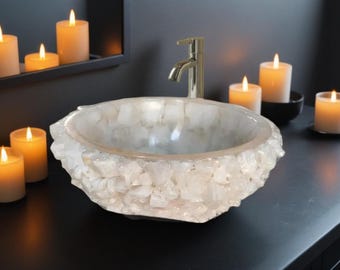 May include: A white crystal quartz sink with a rough, textured exterior and a smooth, polished interior. The sink is set on a black countertop with candles in the background.