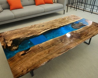 Puede incluir: Una mesa de centro de madera grande con un diseño de borde vivo. La mesa tiene un río de epoxi azul que atraviesa el centro. La mesa está hecha de madera natural y tiene un aspecto rústico.