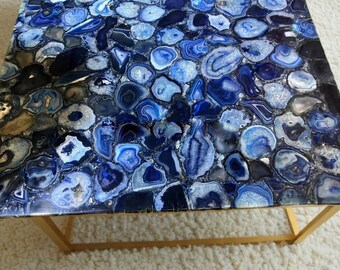 May include: A square coffee table with a blue agate top and a gold metal frame. The agate top features a variety of blue and white patterns.