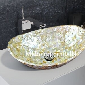 May include: Oval-shaped bathroom sink made of iridescent mother of pearl tiles. The sink is white with gold and brown accents. The sink is on a white countertop.